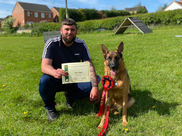 Ronan crouching with his German Shepherd and a training certificate